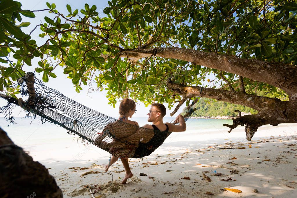 Young tourist couple relaxing on simple hammock on secret beach on Pangkor island in Malaysia. Beautiful seascape and harbor taken in south east Asia.