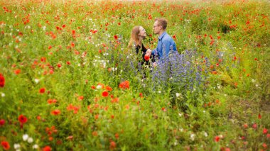 Çekici genç çift güzel bir kırmızı haşhaş tarlasında dinleniyor. Romantik çekim, kırsal alan, doğal çayır, Silezya, Polonya.