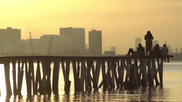 Sylwetka gości siedzieć na końcu drewnianego mostu zrobić zdjęcie — Wideo stockowe