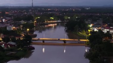 Geceleri içinden nehir akan bir şehir. Su sakin ve şehirden gelen ışıklar suyu yansıtıyor. Hava manzaralı Bandar Baharu, Kedah