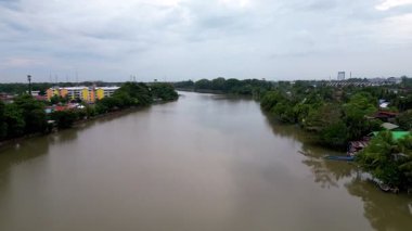 Alor Setar, Kedah, Malezya - Jan 07 2024: Arkasında sarı bir bina bulunan bir nehir. Su kahverengi ve bulanık. Nehrin her iki tarafında da ağaçlar var.