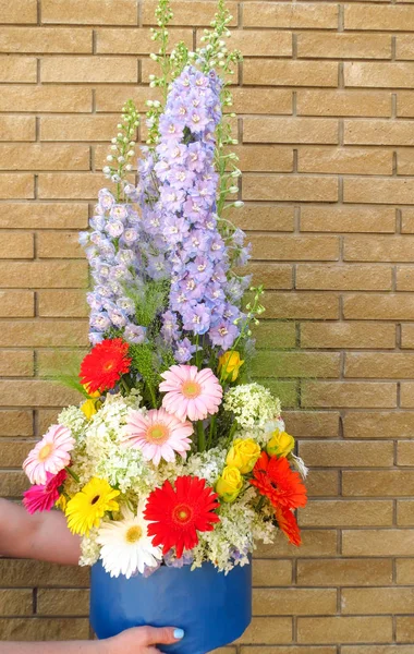 The work of a florist in a flower shop. Summer bouquet with hydrangea, bright chrysanthemum and majestic delphinium plant on a brick wall background