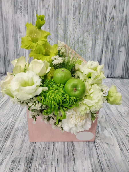 Work in a flower shop - a flower envelope with apples and berries close-up. A beautiful bouquet in a cardboard envelope close-up on a wooden background - an idea for a romantic gift