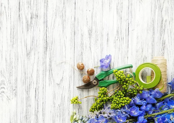 Floral background: blue delphinium and florist tools on wooden background. Secateurs, twine, floristic wire, pets and plants - florist at a flower shop