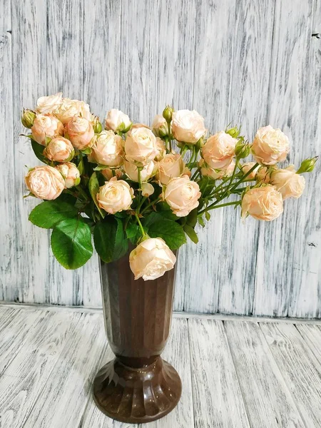 Cream peony roses in a vase closeup on a wooden background. Work in a flower shop. Bouquet of roses