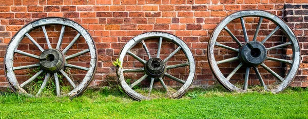 Three old wooden cart wheels against a red brick wall