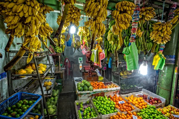 Indoor rural fruit stall in Sri Lanka with hanging bananas and varied selection of fruits on display