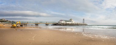7 Şubat 2020 'de Bournemouth, Dorset, İngiltere' deki Bournemouth İskelesi 'nin önündeki sahili kazan bir JCB Kazıcısının panoramik görüntüsü