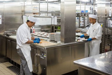 Mutfaktaki yemek hazırlama sahnelerinin ardında, 24 Temmuz 2019 tarihinde Baltık Denizi 'ndeki Kraliçe Victoria' da büyük bir yolcu gemisinde kadırga bulunmaktadır.