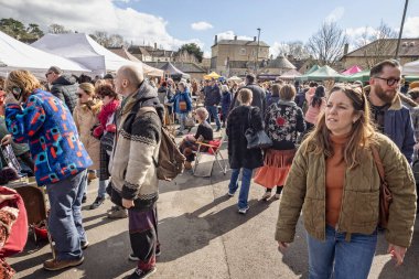 3 Mart 2024 'te İngiltere' nin Somerset kentindeki Frome Independent Sunday Market 'te oturan bayanın önünden kalabalık geçti.