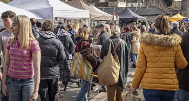 3 Mart 2024 'te İngiltere' nin Somerset kentindeki Frome Independent Sunday Market 'te oturan bayanın önünden kalabalık geçti.