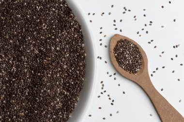 Beyaz arkaplanda beyaz seramik tabakta chia tohumları ve tahta kaşık yakın plan.