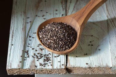 Tahta kaşıkta çim tohumları, açık yeşil ahşap arka planda.