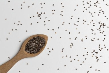 Chia tohumları ve tahta bir kaşık, beyaz arka planda.