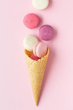 Pastel pembe arka plan üzerinde pastel pasta macaron veya acıbadem kurabiyesi ve tatlı koni Flatlay. Metin alanı olan üstten görünüm