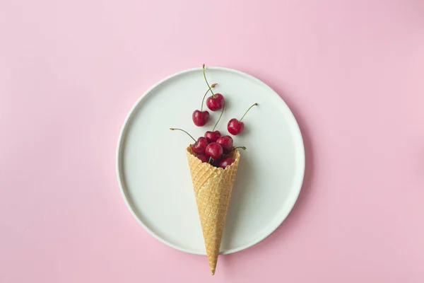 Spring or summer mood concept. Flat-lay of waffle sweet cone with berryy over pastel light pink background, top view.