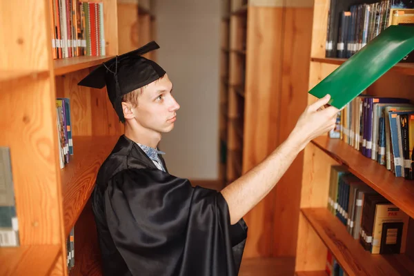 Успішний Аспірант Академічних Сукнях Позує Бібліотеці Тримає Зелену Теку Може — стокове фото