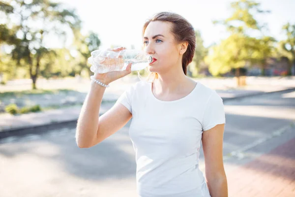Young sports girl, drinking water from the bottle, after a hard workout, can be used for advertising
