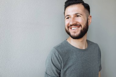 Bir tuğla gri duvar arka plan üzerinde gri bir boş t-shirt duran bir çekici şık adam portresi giymiş.