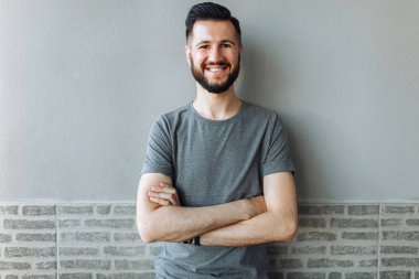 Bir tuğla gri duvar arka plan üzerinde gri bir boş t-shirt duran güzel şık adam portresi giymiş.