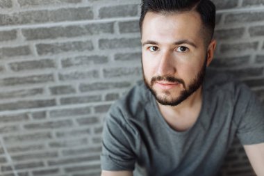 Bir tuğla gri duvar arka plan üzerinde gri bir boş t-shirt duran güzel şık adam portresi giymiş.