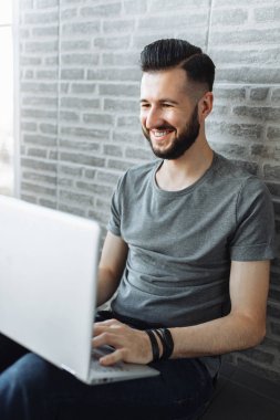 Bir dizüstü bilgisayarda çalışıyor güzel şık birine, bir hipster portresi bir tuğla duvar gri arka plan üzerinde duran bir gri boş t-shirt giyen.