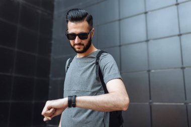 Güzel şık tekiyle saate benzeyen hipster gözlüklü, portre siyah duvar arka plan üzerinde duran bir gri boş t-shirt giymiş.