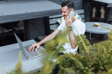 güzel şık adam, sokakta, bir dizüstü bilgisayar üzerinde çalışan ve telefonda konuşurken masadan boş beyaz tişört, yenilikçi, fotoğraf,