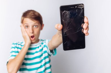 Mavi t-shirt güzel bir portresi ve duygusal çocuk, kimin elinde bir kırık telefon sürpriz, beyaz arka plan, gösterir.,