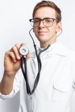 El yakın çekim holding stetoskop, izole beyaz zemin üzerine genç doktor portresi