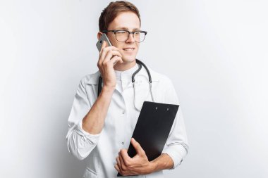 Genç ve yakışıklı doktor hasta ile telefon, stajyer öğrenci klasörle elinde, konuşurken beyaz arka plan,