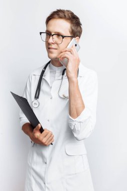 Genç ve yakışıklı doktor hasta ile telefon, stajyer öğrenci klasörle elinde, konuşurken beyaz arka plan,