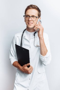 Genç ve yakışıklı doktor hasta ile telefon, stajyer öğrenci klasörle elinde, konuşurken beyaz arka plan,