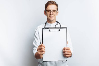 Kamera, beyaz bir arka plan üzerinde bir klasör boş bir levha ile genç bir doktor gösterir,