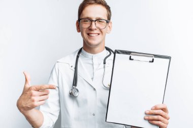 Kamera, beyaz bir arka plan üzerinde bir klasör boş bir levha ile genç bir doktor gösterir,