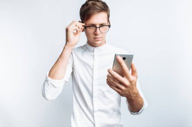 Telefon, beyaz gömlek beyaz arka plan üzerinde izole bakarak gözlüklü genç çekici adam portresi,