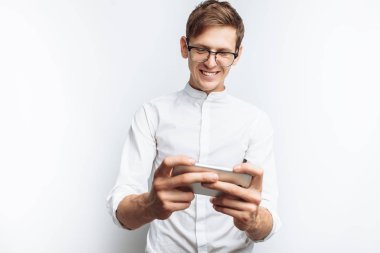 Oyun telefon, beyaz arka plan üzerinde izole beyaz gömlekli gözlüklü genç çekici adam portresi,