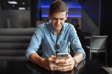 Mutlu genç adam akıllı tarama Internet kafede otururken,