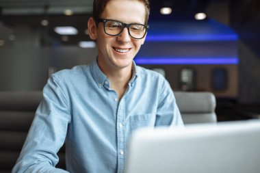 İyi bir ruh hali, bir gömlek ve gözlük, bir kafede bir dizüstü bilgisayar üzerinde çalışan bir iş adamı olan genç bir adam portresi,