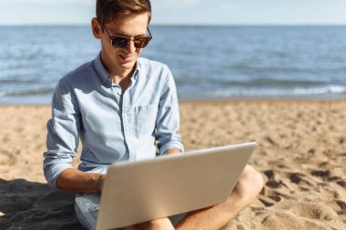 Gözlüklü genç adam, onun laptopunda sahilde çalışma, tatilde çalışma,