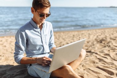Gözlüklü genç adam, onun laptopunda sahilde çalışma, tatilde çalışma,