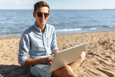 Gözlüklü genç adam, onun laptopunda sahilde çalışma, tatilde çalışma,
