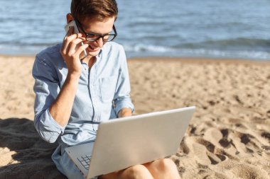 Gözlüklü, onun laptop çalışma ve tatilde çalışma sahilde, telefonda konuşurken genç adam,