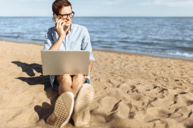 Gözlüklü, onun laptop çalışma ve tatilde çalışma sahilde, telefonda konuşurken genç adam,