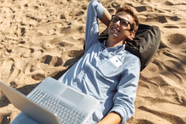 Gözlüklü, Genç adam tatilde çalışma karşı deniz, plaj onun laptop üzerinde kum üzerinde yalan,