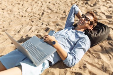 Gözlüklü, Genç adam tatilde çalışma karşı deniz, plaj onun laptop üzerinde kum üzerinde yalan,