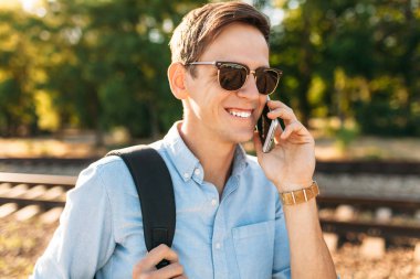 Tren rayları üzerinde günbatımında poz ve telefon, şık giysiler içinde poz hipster konuşmak güzel şık gözlüklü,,