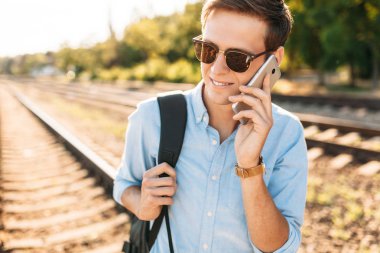 Tren rayları üzerinde günbatımında poz ve telefon, şık giysiler içinde poz hipster konuşmak güzel şık gözlüklü,,