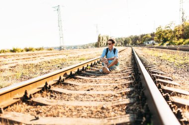 Gün batımı, yenilikçi şık giysiler içinde poz, tren rayları üzerinde oturan poz güzel şık gözlüklü,,