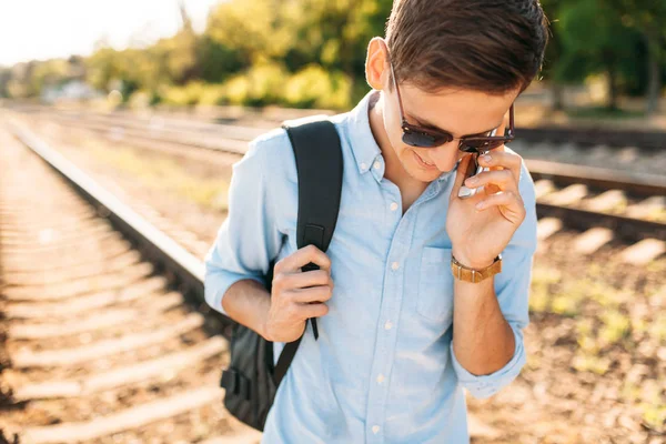 Tren rayları üzerinde günbatımında poz ve telefon, şık giysiler içinde poz hipster konuşmak güzel şık gözlüklü,,